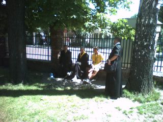 Na dziedzińcu kościółka pw. Przemienienia Pańskiego ciało duchowne (ks. Jan Plottke, ks. kierownik i stojący ks. Daniel) i porządkowy Piotr wyczekują pielgrzymki…